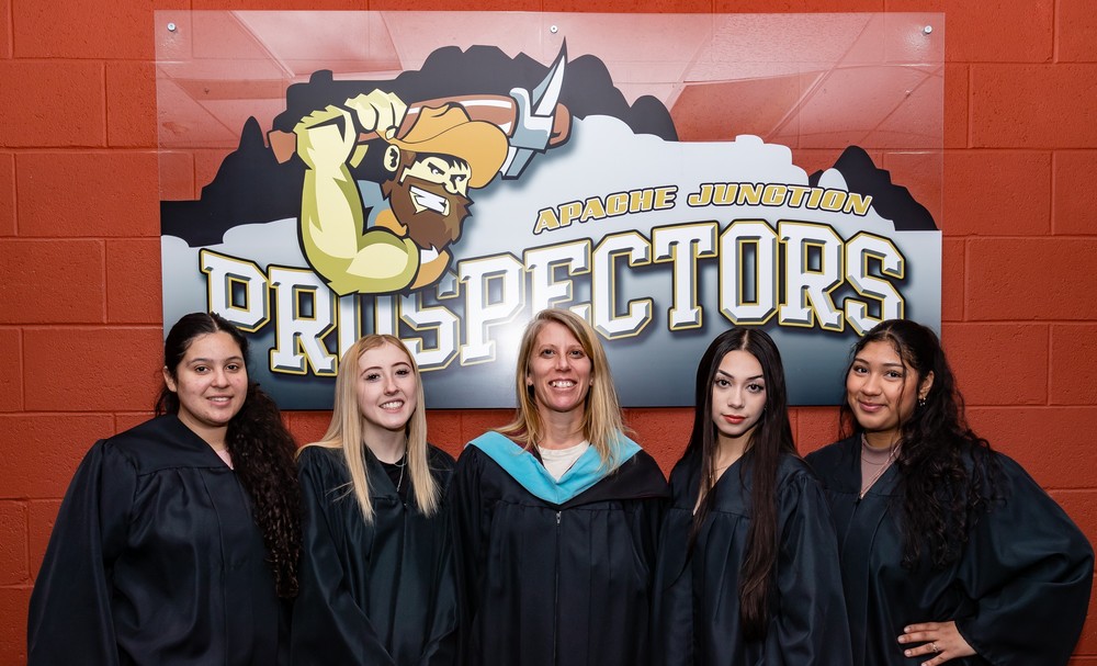 4 students 1 teacher in graduation robes by prospectors sign